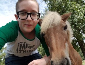 Image of Courtney Kirkham in a MapThis! t-shirt standing next to a miniature horse.