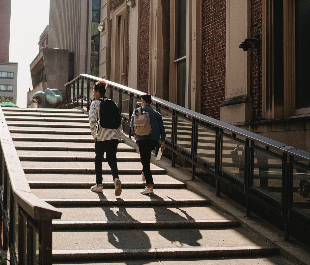 Two individuals with backpacks walking away from the photographer. They are going up stairs with a gradual incline.